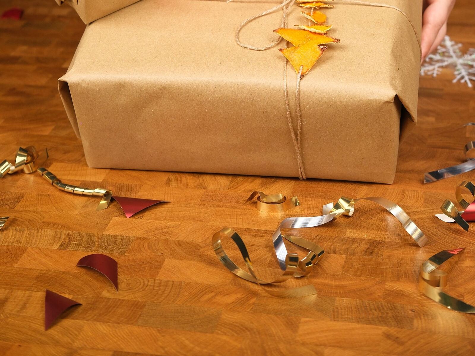 A gift wrapped in kraft paper and twine with gold ribbon curls on a wooden table