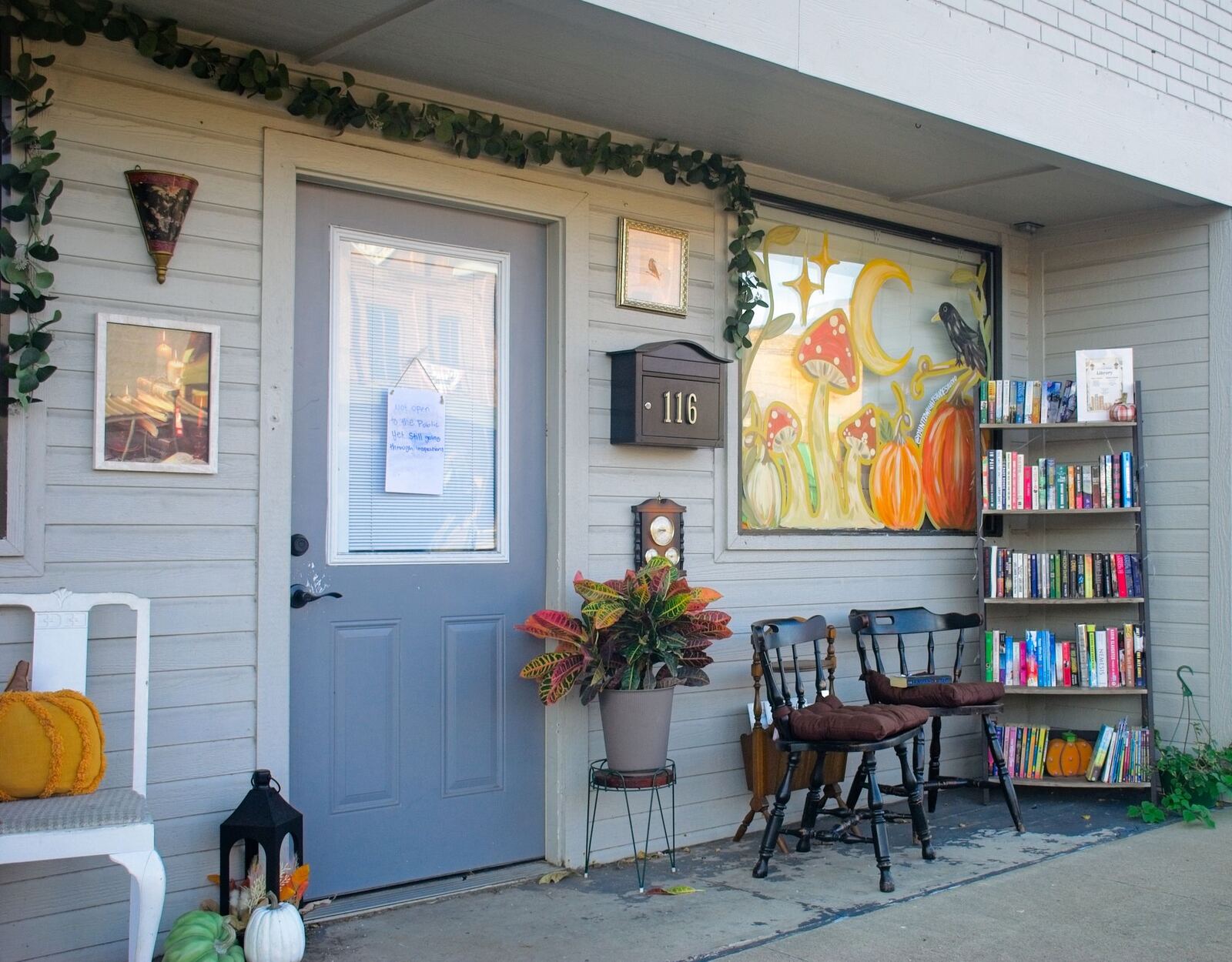 The shop’s front porch dressed for fall, with pumpkins, a bookshelf and two chairs by the door